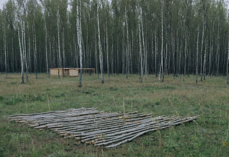 Пустой участок с колышками разметки под дом и штабелем бруса на краю